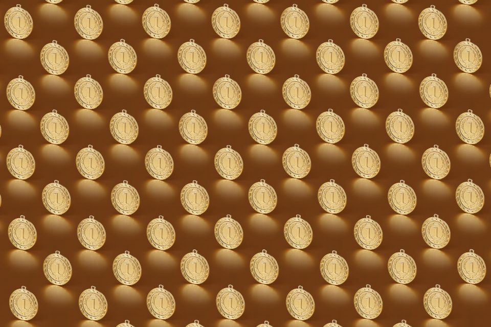 Multiple gold medals arranged in a repeating pattern on a brown backdrop.