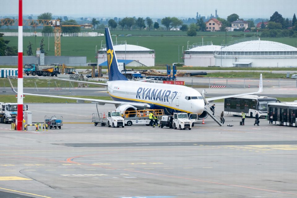 Passengers and crew prepare a Ryanair plane for departure at a bustling airport terminal.
